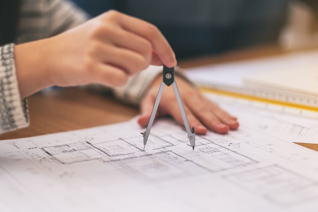 An architect using compass to draw and measure shop drawing in office