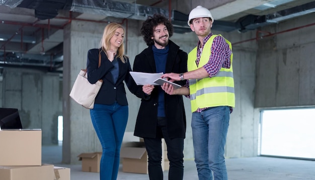 architect using tablet computer while showing house design plans to a young couple at construction site