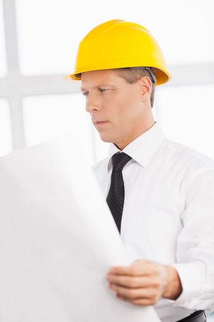 Architect with blueprint. Confident senior man in formalwear and hardhat holding a blueprint and looking at it
