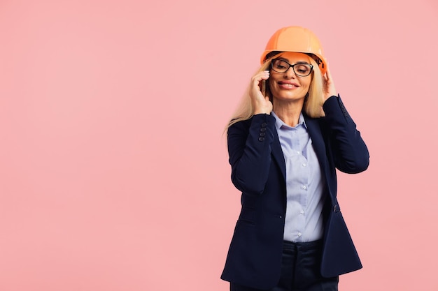 Architect woman in glasses use mobile phone call with engineer\
or project manager on the pink background