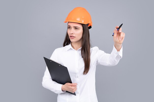 Architect woman in helmet pointing young woman in helmet hold\
clipboard on gray background