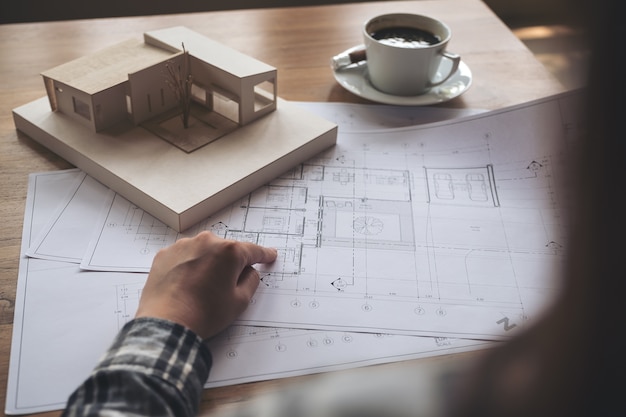 Un architetto che lavora su un modello di architettura con carta da disegno negozio e tazza di caffè