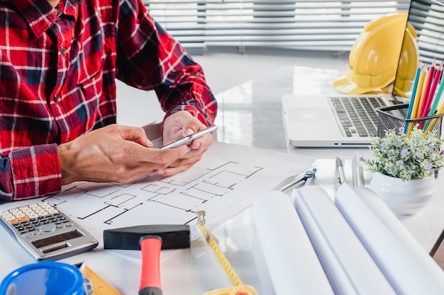 Architect working on blueprint with\
blueprints,ruler,calculator,laptop and divider compass