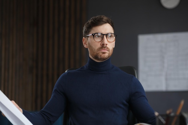 Architect working in office with blueprints.Engineer inspect architectural plan, sketching a construction project.Portrait of handsome bearded man sitting at workplace. Business construction concept.