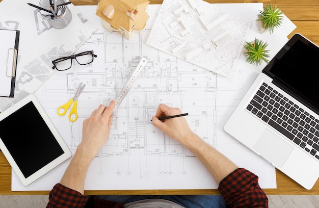 Architect working with blueprints in modern workplace interior, top view, copy space. Interior designer's working table, an architectural plan of the house.