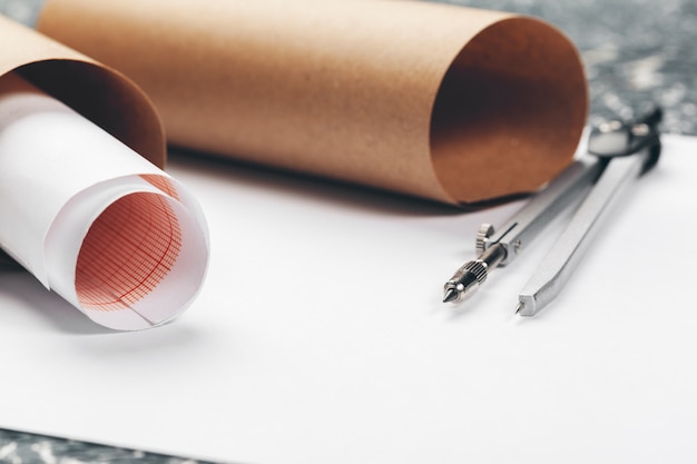 Architectural blueprints and blueprint rolls and a drawing instruments on the worktable.