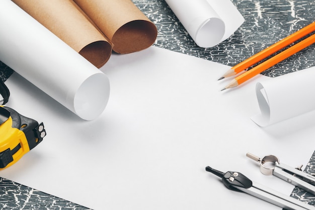 Architectural blueprints and blueprint rolls and a drawing instruments on the worktable. 