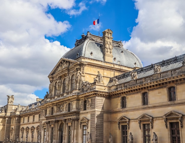 Architectural details of the facade of the Louvre in Paris with the French flag on the roof