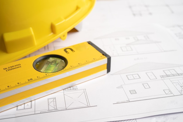 Architectural house plan project blueprint with yellow helmet\
and engineering construction tools