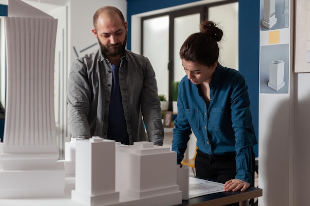 Architecturale ingenieurs die teamwerk doen en bouwplannen lezen die naast de tafel staan met maquette van schuimmodel. Team van twee architectencollega's die samenwerken die blauwprinsen bekijken.