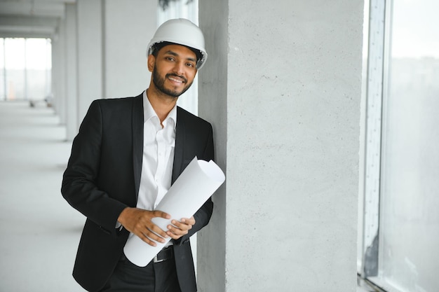 建築建設事業と建物のコンセプト ヘルメットで幸せな笑みを浮かべてインドの男性建築家