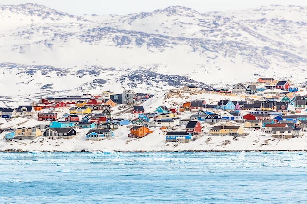 雪と雪に覆われた岩の多い丘の上にカラフルなイヌイットの家がある北極都市のパノラマ