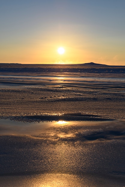 Arctic landscape in winter time. Small river with ice in tundra. Sunset.