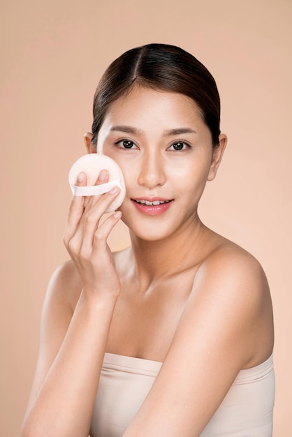 Ardent woman applying her cheek with dry powder while looking at camera