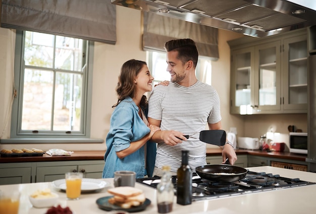 Are you trying to score some brownie points Shot of a young woman embracing her partner while he cooks breakfast