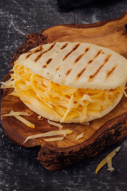 Arepa met gele kaas op een houten bord. (Arepa Catira)