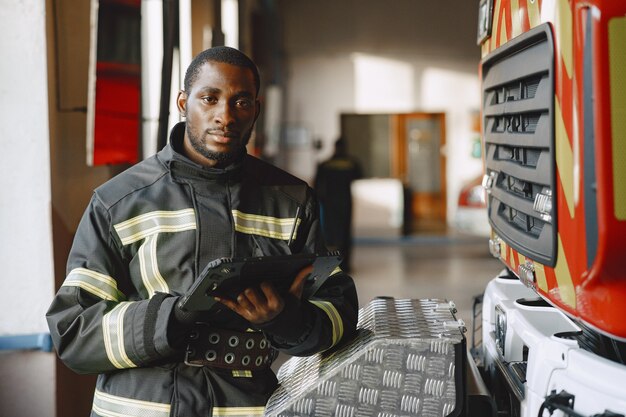 Vigile del fuoco arfican in uniforme. l'uomo si prepara a lavorare. ragazzo con tablet.