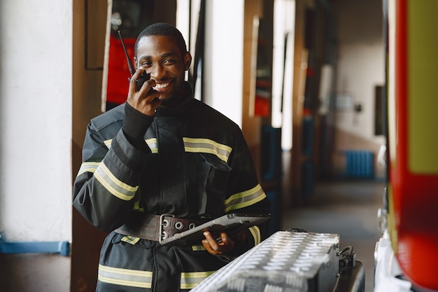 Vigile del fuoco arfican in uniforme. l'uomo si prepara a lavorare. ragazzo con tablet.