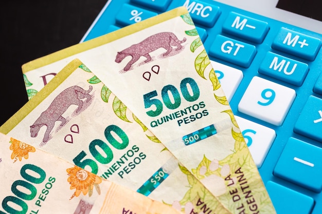 Argentine peso banknotes and a calculator in closeup photo.