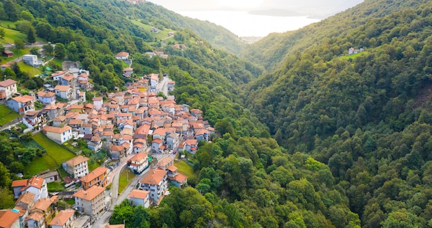 Arial view on mountain Italian village, Garzeno. High angle view of houses with red roofs among trees on the top of the mountain in summer.