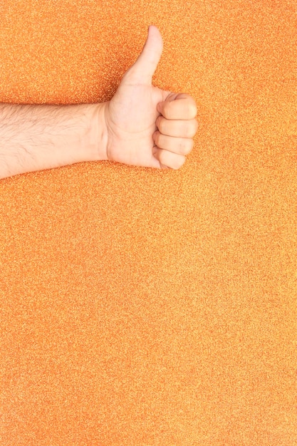 Arm with thumb up hand gesture on top with glitter orange background