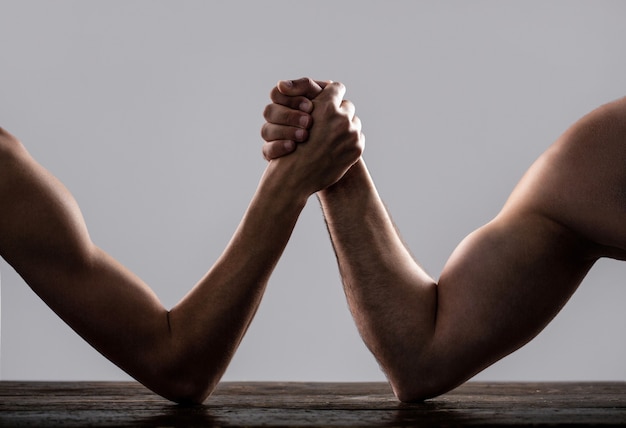 Arm wrestling. Heavily muscled man arm wrestling a puny weak man.