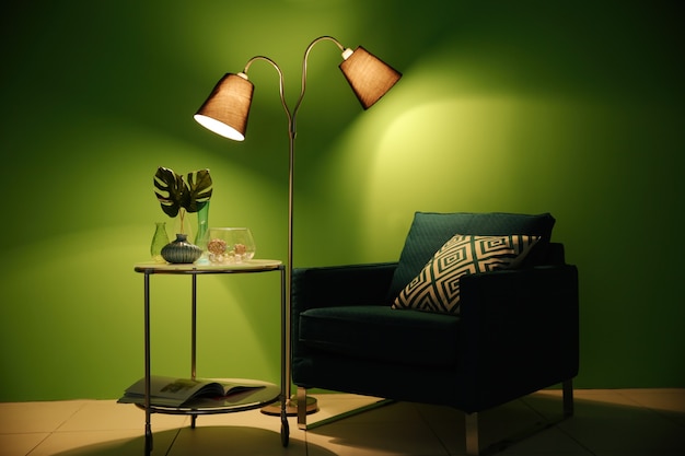 緑の壁の表面に家の装飾が施されたアームチェア、ランプ、テーブル