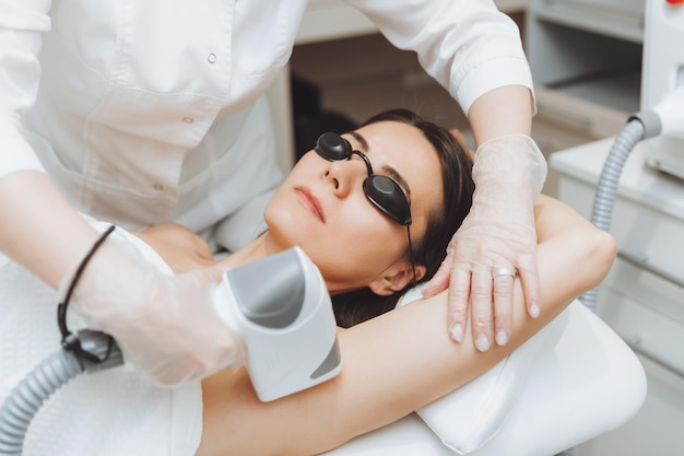 Depilazione laser per ascelle cosmetologo che rimuove i peli delle ascelle di una giovane donna depilazione laser nella clinica di bellezza estetica il concetto di salute e bellezza