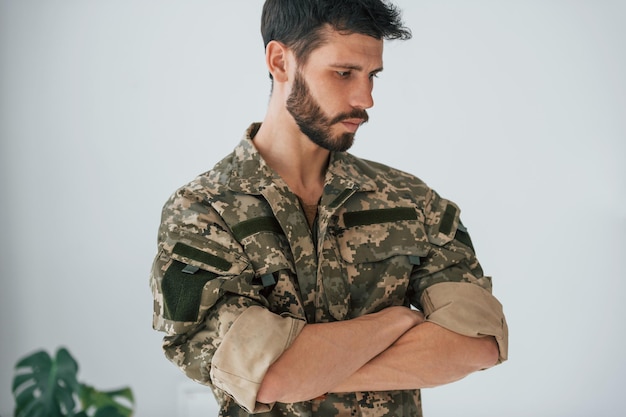 Foto braccia incrociate il soldato in uniforme è in piedi al chiuso contro il muro bianco