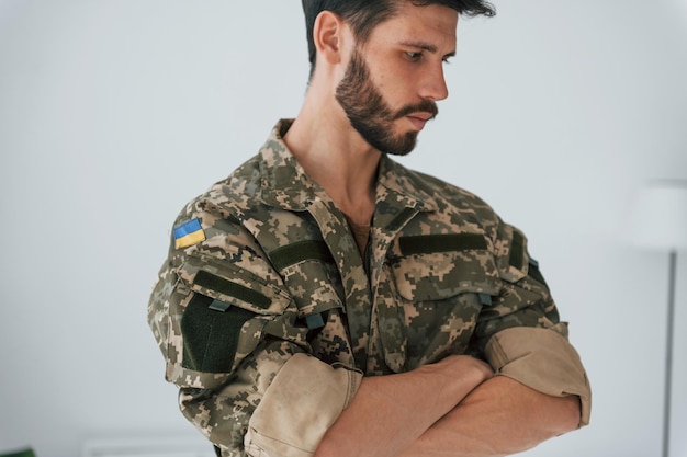 Arms crossed Soldier in uniform is standing indoors against white wall