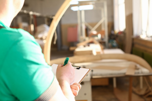 Arms of worker making notes on clipboard with green pen