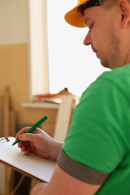 Arms of worker making notes on clipboard with green pen