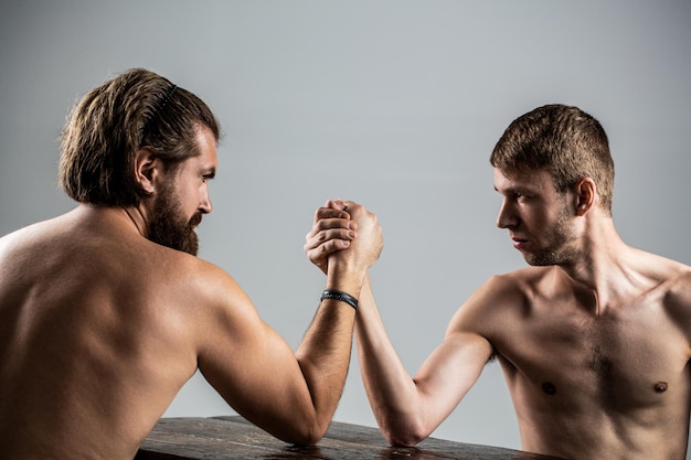 Photo arms wrestling thin hand big strong arm in studio two man's hands clasped arm wrestling strong and weak unequal match arm wrestling heavily muscled bearded man arm wrestling a puny weak man