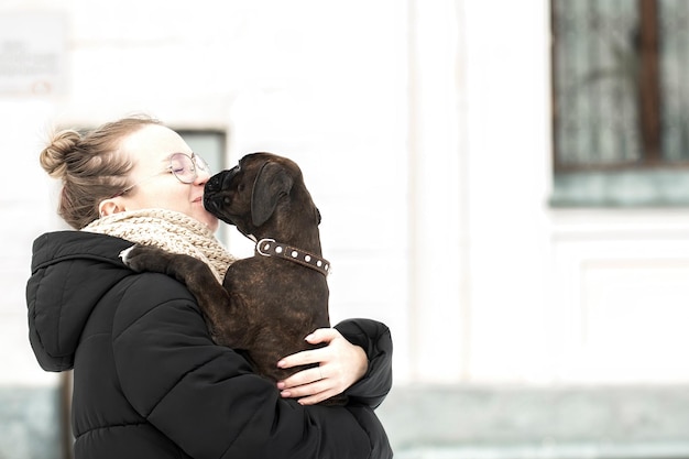 На руках у молодой женщины ее любимый щенок немецкого боксера на прогулке