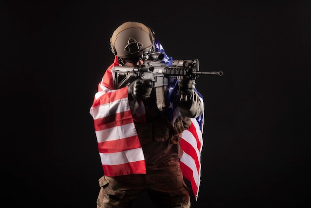 미국 육군 총을 든 군사 장비를 입은 군인이 검은 배경에 미국 국기를 들고 있다