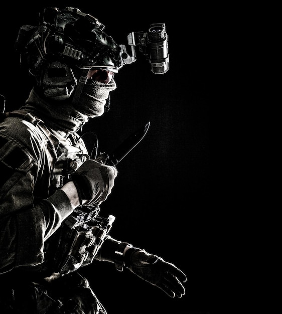 Army elite commando professional mercenary counterterrorist tactical team fighter in combat helmet equipped nightvision device creeping in darkness with service knife in hand studio shoot