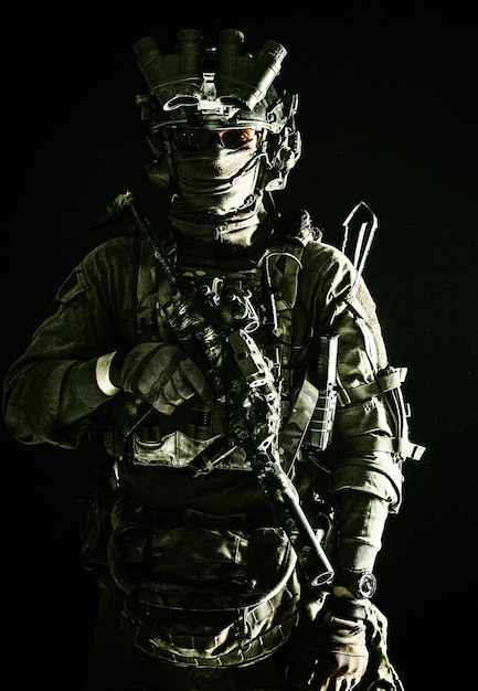 Army elite troops serviceman counterterrorist team member\
wearing mask and glasses equipped nightvision device radio headset\
mounted on combat helmet armed submachine gun standing in\
darkness