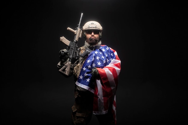 Фото Армия америки солдат в военной технике с ружьем держит флаг сша на черном фоне