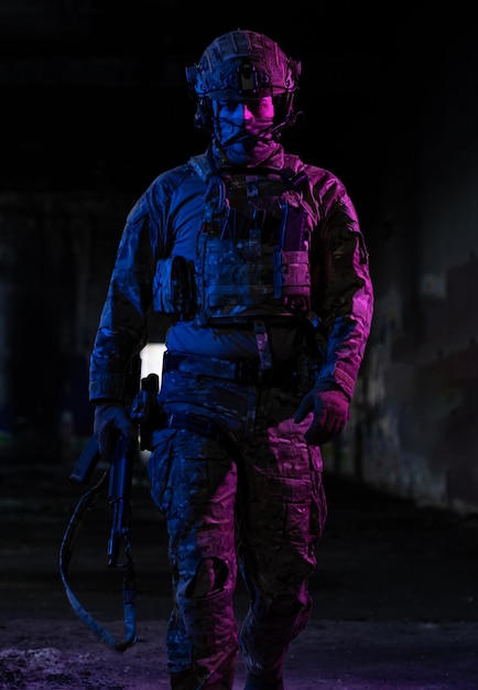 Army soldier in Combat Uniforms with an assault rifle and combat helmet night mission dark background. Blue and purple gel light effect. High quality photo