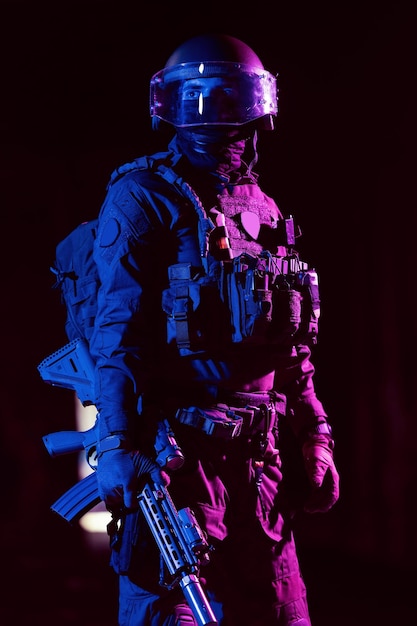 Армейский солдат в боевой форме с штурмовой винтовкой и боевым шлемом на темном фоне ночной миссии. Эффект синего и фиолетового геля. Фото высокого качества