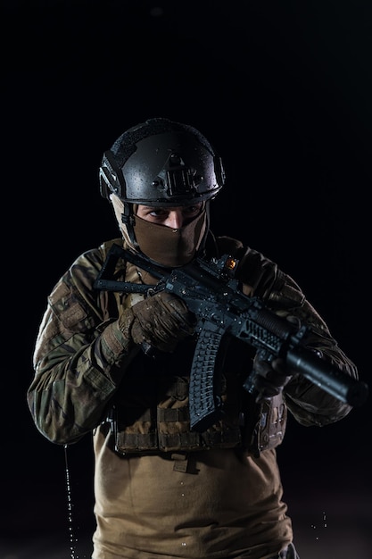 Army soldier in Combat Uniforms with an assault rifle, plate carrier and combat helmet going on a dangerous mission on a rainy night. High quality photo