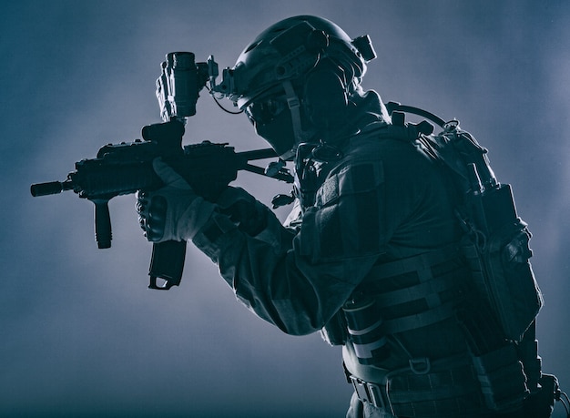 Army soldier, counter terrorist squad fighter, military company mercenary in ammunition and body armor, helmet with night vision device, aiming with short barrel service rifle, low key, studio shoot