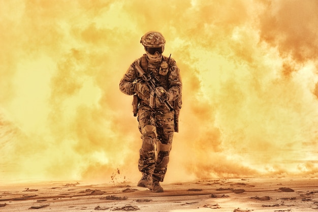 Army soldier in military camouflage uniform, helmet, with face hiding behind mask and glasses, running out from fire. Infantry rush with fire support, commando attack and breakthrough on battlefield