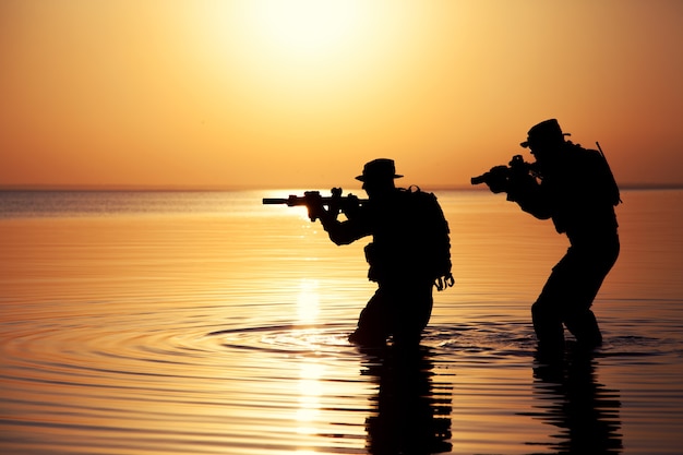 ライフルのオレンジ色の夕日のシルエットを持つ陸軍兵士