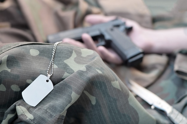 Army token lies on camouflage uniform of dead soldier and hand with pistol. Concept of war actions between East Ukraine and Russia