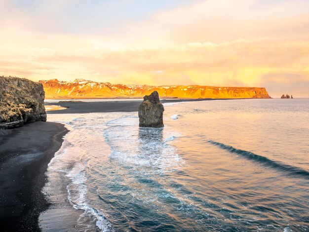Арнардрангур на береговой линии возле арки Дирхолаей, окруженной горой с тяжелыми волнами к югу от Исландии