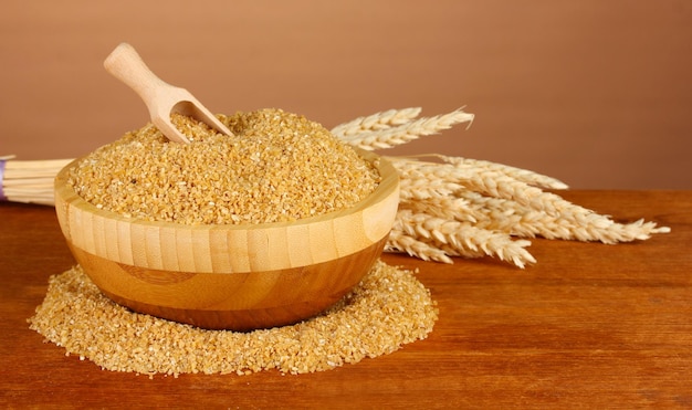 Photo arnautka in wooden bowl with spikelets on brown background closeup