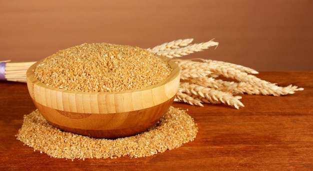 Arnautka in wooden bowl with spikelets on brown background closeup