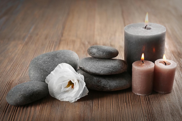 Aroma candle with pebbles and flower on wooden background