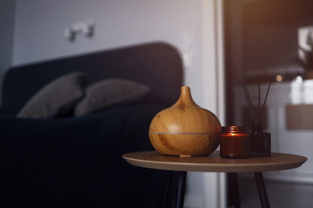 Diffusore di oli aromatici, deodorante per ambienti e candela su un tavolo di legno in camera da letto. fotografia calda e d'atmosfera.